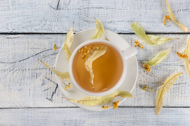 top view of a white cup linden tea or blooming tilia, basswood, on rustic vintage white wooden table. herbal tea concept, selective focus - alternative medicine herb garden plant flower imagens e fotografias de stock