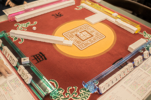 Table where Mahjong - the Mandarin tile-based game - is being played on a colorful mahjong mat with a dice in the middle - selective focus