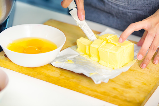 Female hands cutting butter next to a bowl of eggs during cake preparation