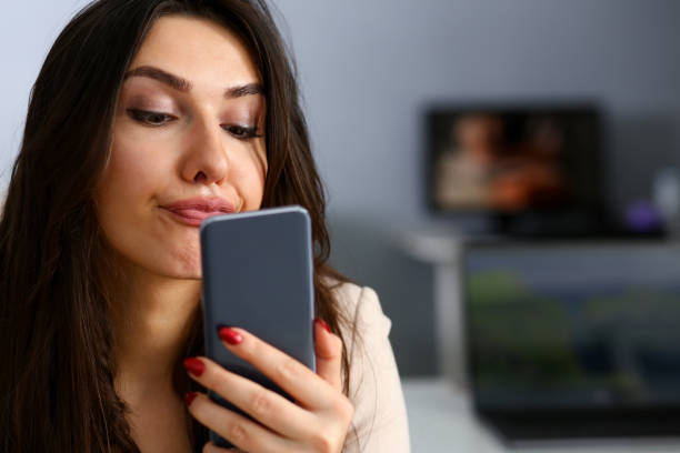 Young beautiful businesswoman unhappily holding Young beautiful businesswoman unhappily holding smartphone in her hand contemptuously looks at display boyfriend stock pictures, royalty-free photos & images
