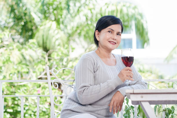 two stylish senior women in pink sweaters with rose wine glasses on pink background. Friendship, talk, gossip, mature female friendship, relationships, news, family concept