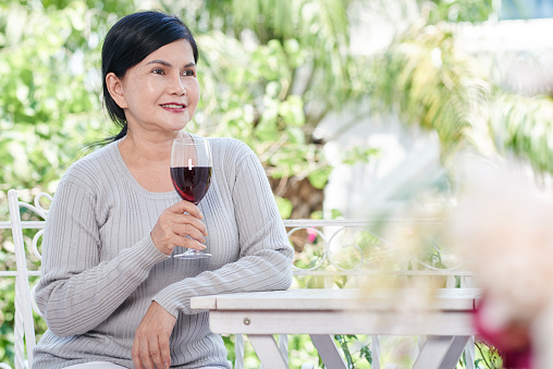 Smiling old woman drinking red wine when resting outdoors