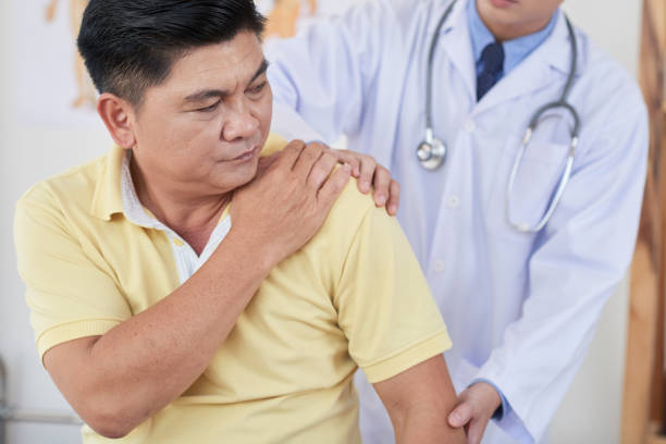 Suffering from pain in shoulder Senior Asian man visiting doctor as he is suffering from pain in shoulder shoulder stock pictures, royalty-free photos & images