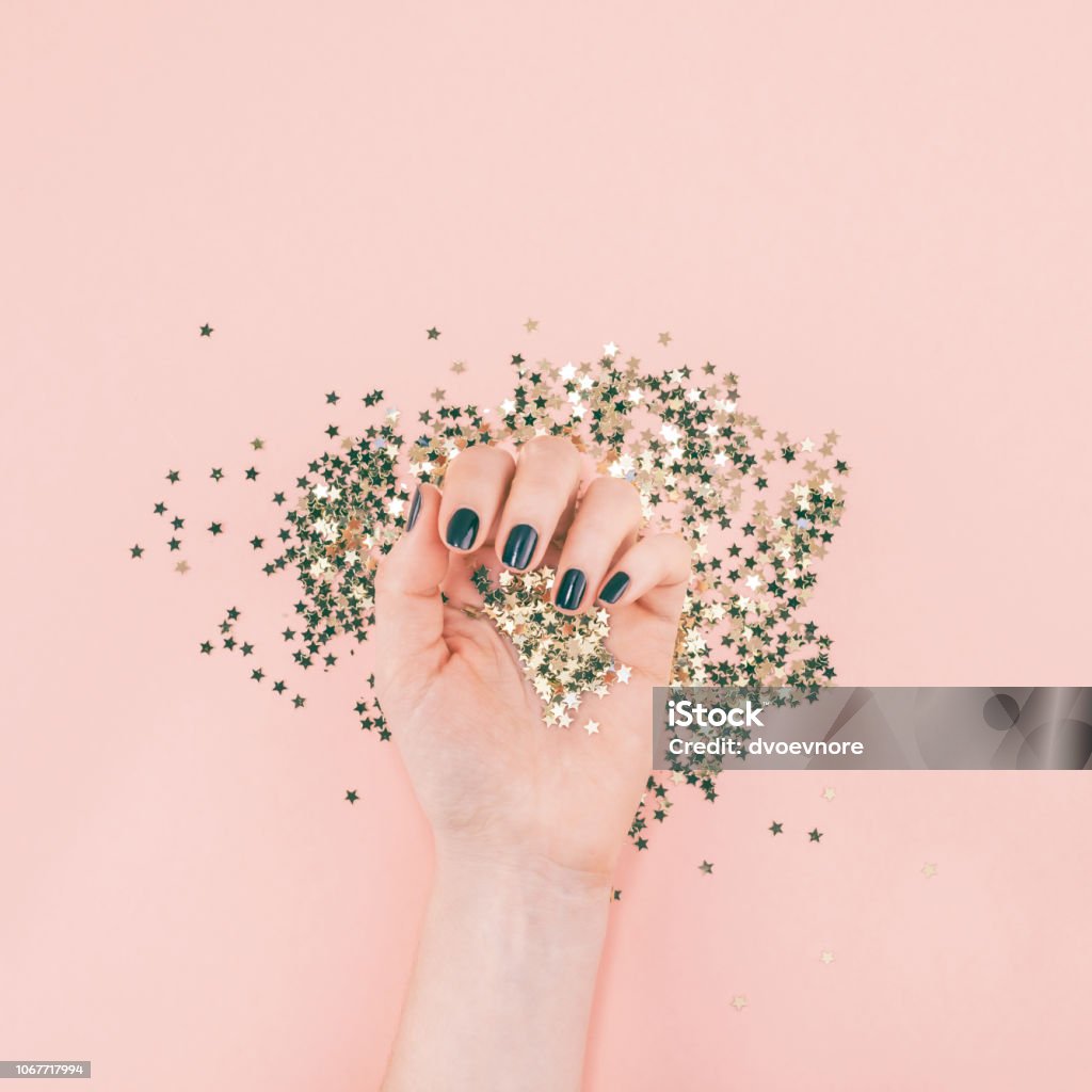 Woman hands covered golden stars confetti on pink New Year or Christmas Top view of woman hands black manicure covered golden stars confetti with copy space millennial pink color paper background minimal style. Template for feminine blog social media Nail Polish Stock Photo