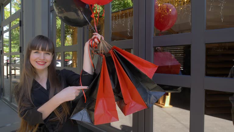 black Friday, girl after shopping with balloons shows of finger on bags with purchases