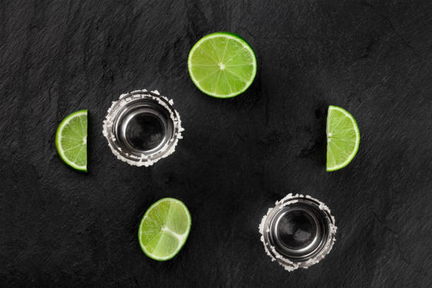 photo de photos de tequila avec limes, tiré par le haut sur un fond noir, formant un cadre avec la place pour le texte - shot glass glass black empty photos et images de collection