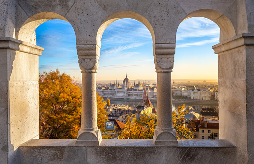 Budapest, Hungary - The beautiful Hungarian Parliament building through old windows of Buda District at sunrise with autumn foliage