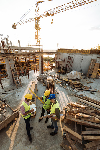 Construction industry concept - architects and engineers discussing work progress between concrete walls, scaffolds and cranes.