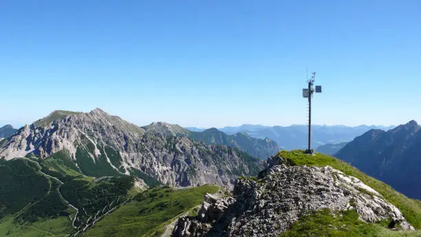 green and rocky mountain landscape in the Swiss Alps with a weather station on a rocky peak for measuring weather data and information in the Davos region on a clear summer dday under a blue sky