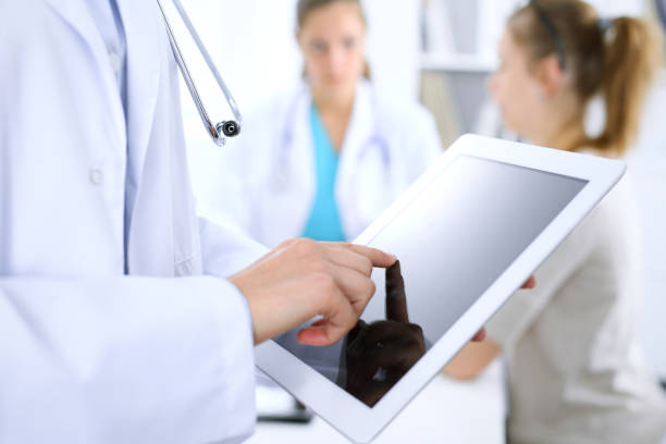 istock Doctor using tablet computer, close-up of hands at touch pad screen. Patient is at the background. 1067782522