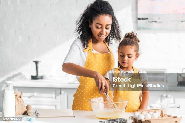 Madre Afroamericana E Hija Preparar La Masa Y Batir Huevos En Cocina Foto de stock y más banco de imágenes de Cocinar