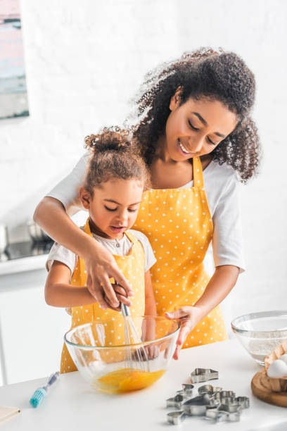 アフリカ系アメリカ人の母と娘が台所で生地の卵を一緒に whisking - preschooler child offspring purity ストックフォトと画像