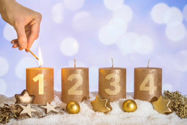 Lit first advent candle in snow by match in hand Four numbered gold advent candles with first candle lit by hand with match and christmas decoration lying in snow as template unlit match stock pictures, royalty-free photos & images