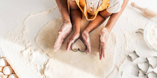 cropped image d’une mère afro-américaine et biscuits préparation fille avec coeur en forme de moule dans cuisine - preschooler child offspring purity photos et images de collection