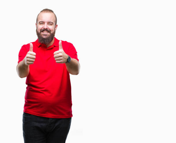 istock Young caucasian hipster man wearing red shirt over isolated background approving doing positive gesture with hand, thumbs up smiling and happy for success. Looking at the camera, winner gesture. 1067799256