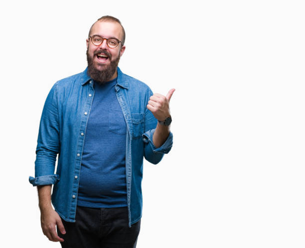 Young caucasian hipster man wearing glasses over isolated background smiling with happy face looking and pointing to the side with thumb up. Young caucasian hipster man wearing glasses over isolated background smiling with happy face looking and pointing to the side with thumb up. overweight man stock pictures, royalty-free photos & images