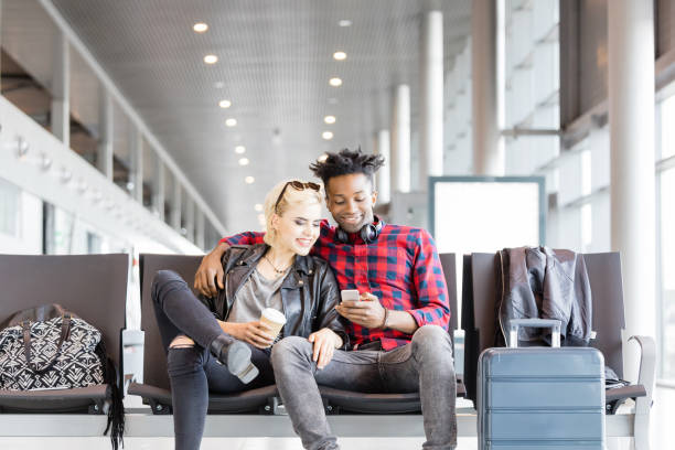 istock Young funky couple using mobile phone in airport lounge 1067803222