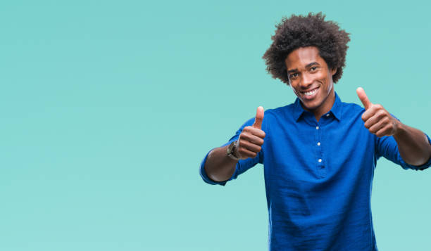 istock Afro american man over isolated background approving doing positive gesture with hand, thumbs up smiling and happy for success. Looking at the camera, winner gesture. 1067803268