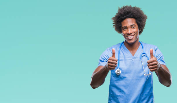 istock Afro american surgeon doctor man over isolated background approving doing positive gesture with hand, thumbs up smiling and happy for success. Looking at the camera, winner gesture. 1067803494