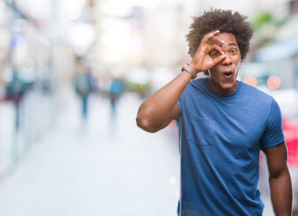 istock Afro american man over isolated background doing ok gesture shocked with surprised face, eye looking through fingers. Unbelieving expression. 1067804956