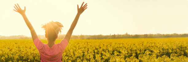 bannière web panoramique de race mixte fille afro-américaine femelle jeune femme athlète coureur adolescent dans les bras de coucher ou lever du soleil d’or posées célébrant en champ de fleurs jaunes - yellow flowers flash photos et images de collection