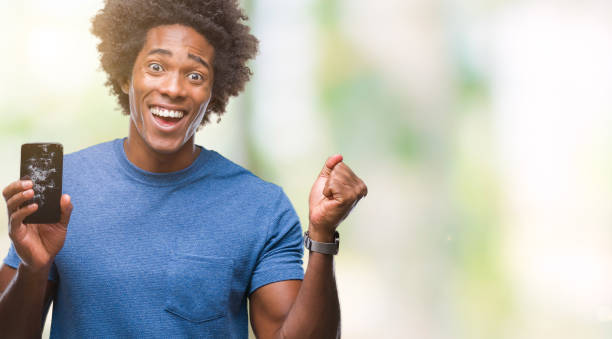 istock Afro american man holding broken smartphone over isolated background screaming proud and celebrating victory and success very excited, cheering emotion 1067805552
