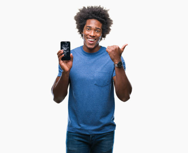 Afro american man holding broken smartphone over isolated background pointing and showing with thumb up to the side with happy face smiling
