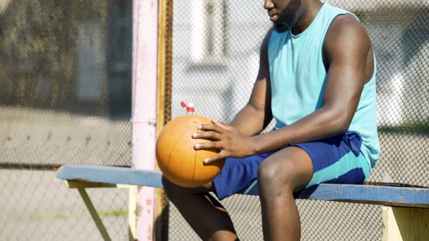 istock Lonely black man sitting alone on bench, playing ball and thinking about friends 1067806924
