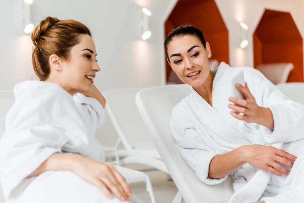 istock smiling young women looking at smartphone while resting together on sunbeds in spa 1067809252