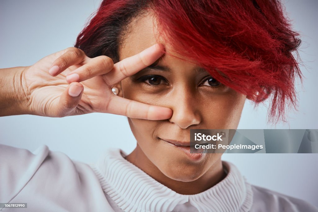 Be unafraid to be yourself Studio shot of a beautiful young woman showing the peace gesture over her eye Biting Lip Stock Photo