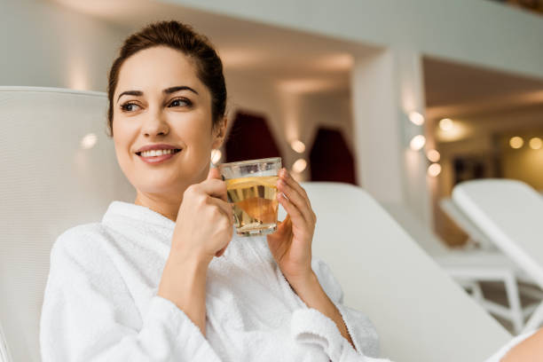 istock beautiful smiling young woman in bathrobe holding cup with herbal drink while relaxing in spa 1067814342