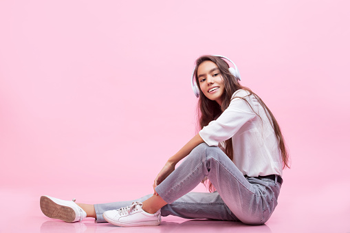 Model young trendy beautiful girl with natural make-up with headphones on a pink background fashion Studio shot