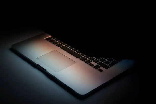Photo of Half closed laptop with screen light on black background