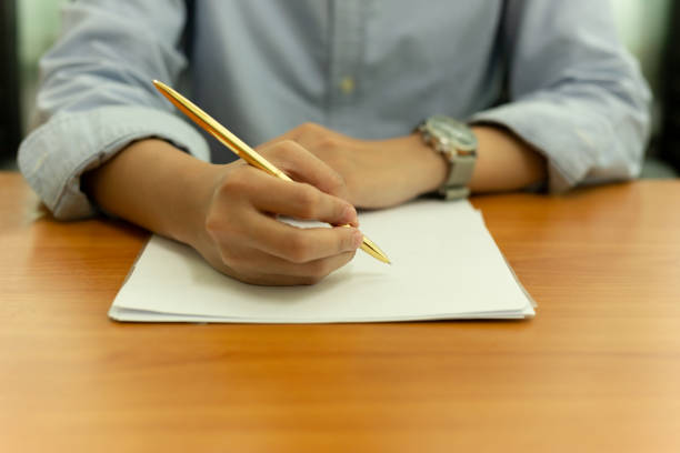 istock Female hand with pen writing on document form on wooden table. 1067840958