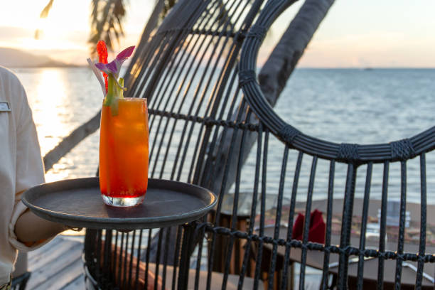 Waiter serving glass of cocktail on the tray by the beach at sunset.