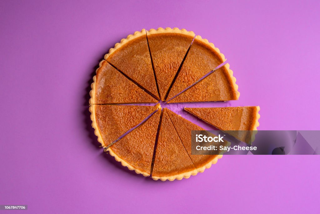 Sliced pumpkin pie and a separate piece. Top view. Traditional dessert Above view of a pumpkin pie cut in slices with one piece separated, on a purple background. Minimalist food image. Thanksgiving traditional dessert. Slice of Food Stock Photo