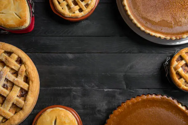 Kitchen table full of different pies, pumpkin pies, apple pies, with empty space in the middle. Traditional holidays dessert. Sweet pastry baking.