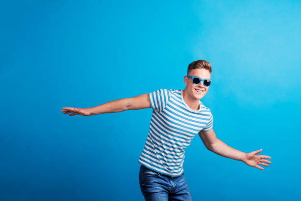 a young man with blue sunglasses standing in a studio, having fun. - retro revival fun caucasian one person imagens e fotografias de stock
