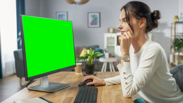 istock Beautiful Young Girl Works on a Green Mock-up Screen Personal Computer while Sitting at Her Desk in the Cozy Apartment. 1067853988