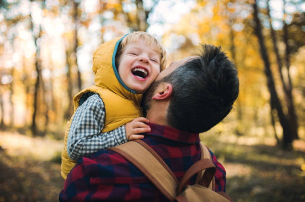 un padre maturo che tiene in braccio un figlio bambino in una foresta autunnale, divertendosi. - fun time foto e immagini stock