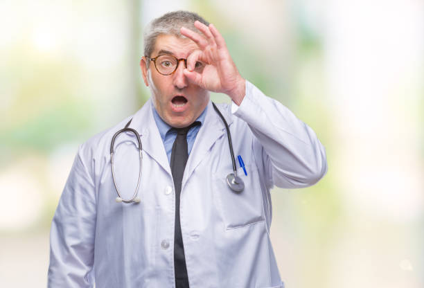 istock Handsome senior doctor man over isolated background doing ok gesture shocked with surprised face, eye looking through fingers. Unbelieving expression. 1067861464