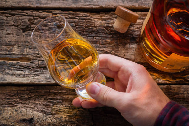 mano sostiene el whisky en una copa para la degustación en un fondo de madera - saborear fotografías e imágenes de stock
