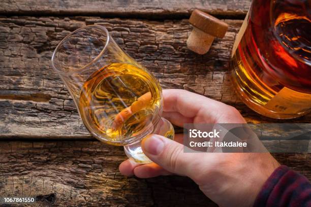 Hand Holds Whiskey In A Glass For Tasting On A Wooden Background Stock Photo - Download Image Now