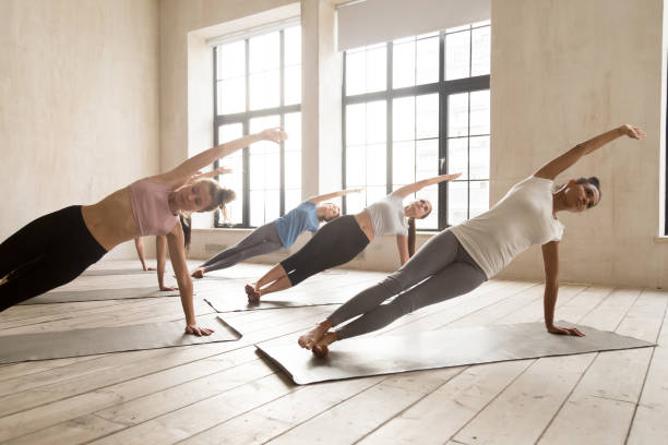 grupa kobiet praktykujących lekcję jogi robi side plank stanowią - posture women side view yoga zdjęcia i obrazy z banku zdjęć