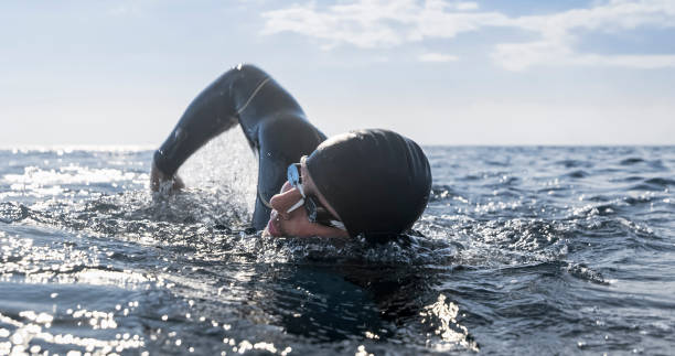 Open water swimmer swimming in sea Male open water swimmer swimming forward crawl in sea. neoprene photos stock pictures, royalty-free photos & images