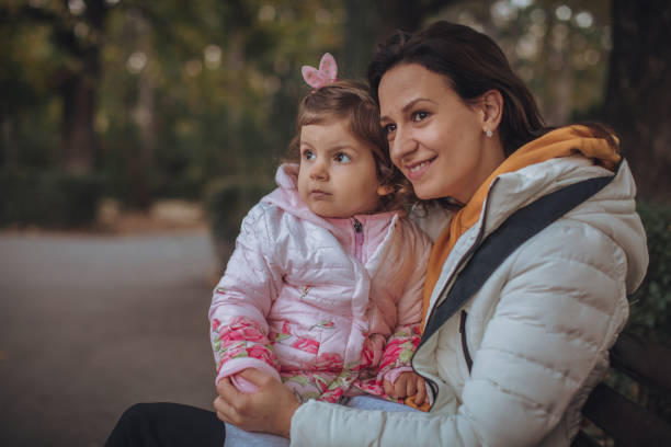 istock Mother and cute daughter sitting in park 1067887152