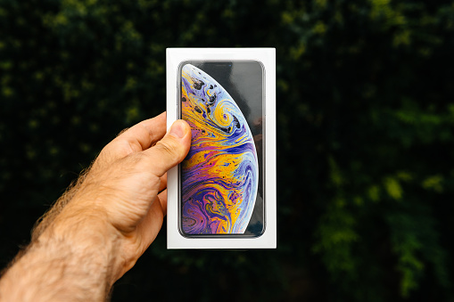 PARIS, FRANCE - SEP 21, 2018: Proud man customer POV comparing the new latest iPhone Xs Max smartphone telephone before the unboxing against green background