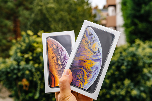 PARIS, FRANCE - SEP 21, 2018: Proud man customer POV comparing the new latest iPhone Xs and Xs Max smartphones telephones before the unboxing against green background