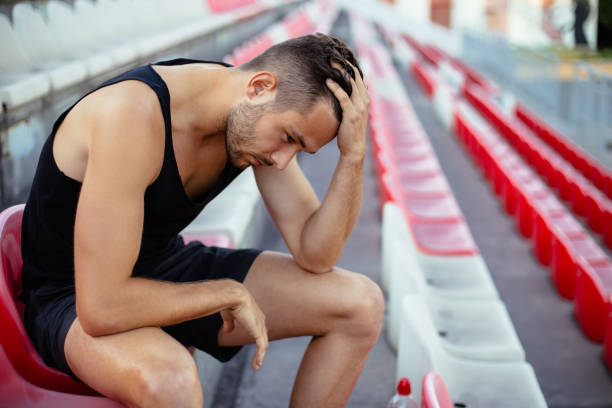 hombre deportista deprimido sentado cabeza en las manos en los asientos del estadio - mens track fotos fotografías e imágenes de stock