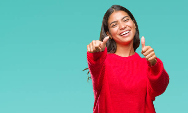 istock Young beautiful arab woman wearing winter sweater over isolated background approving doing positive gesture with hand, thumbs up smiling and happy for success. Looking at the camera, winner gesture. 1067904408